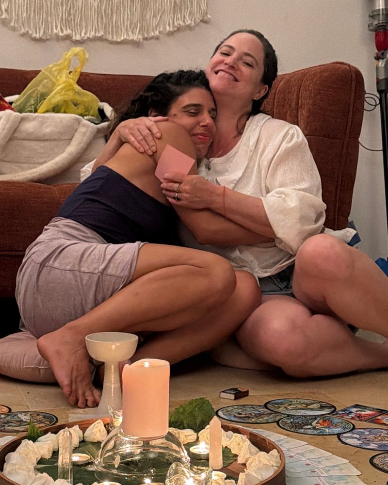 שתי חברות מתחבקות על הספה, מחזיקות פתק ברכה, ומולן מגש הנרות
