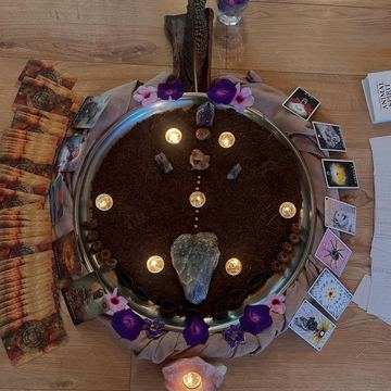 A circle of candles and flowers around a tray with crystals and cards