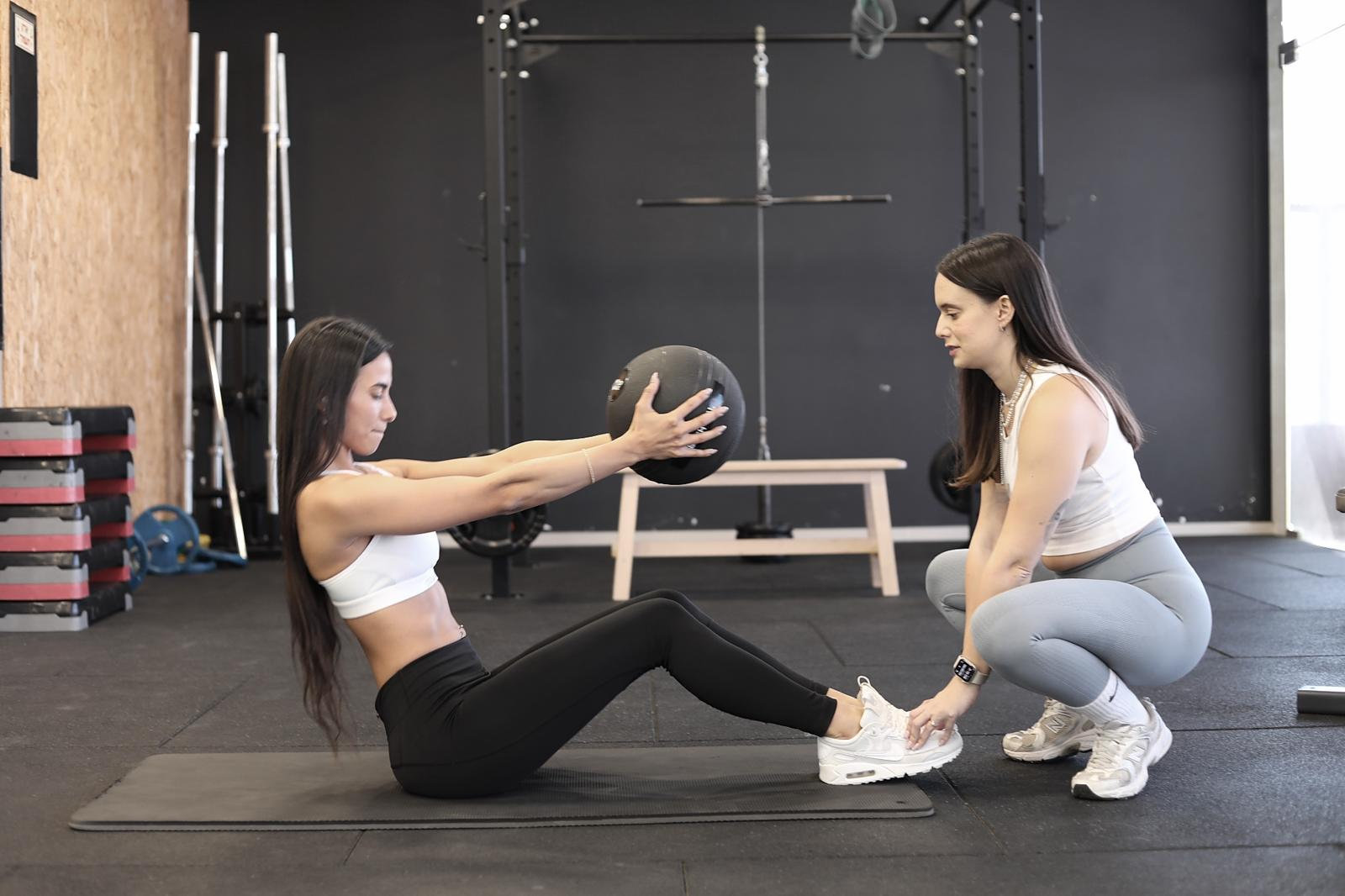 Juli kneeling beside a client doing sit-ups with a medicine ball, holding her feet