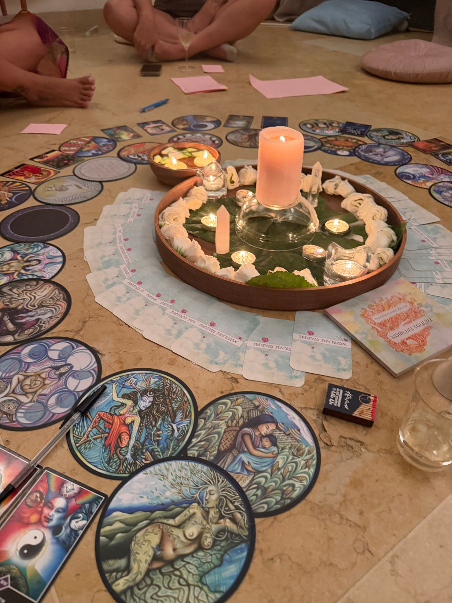 A circle of cards and candles on the floor around a tray of white flowers and crystals
