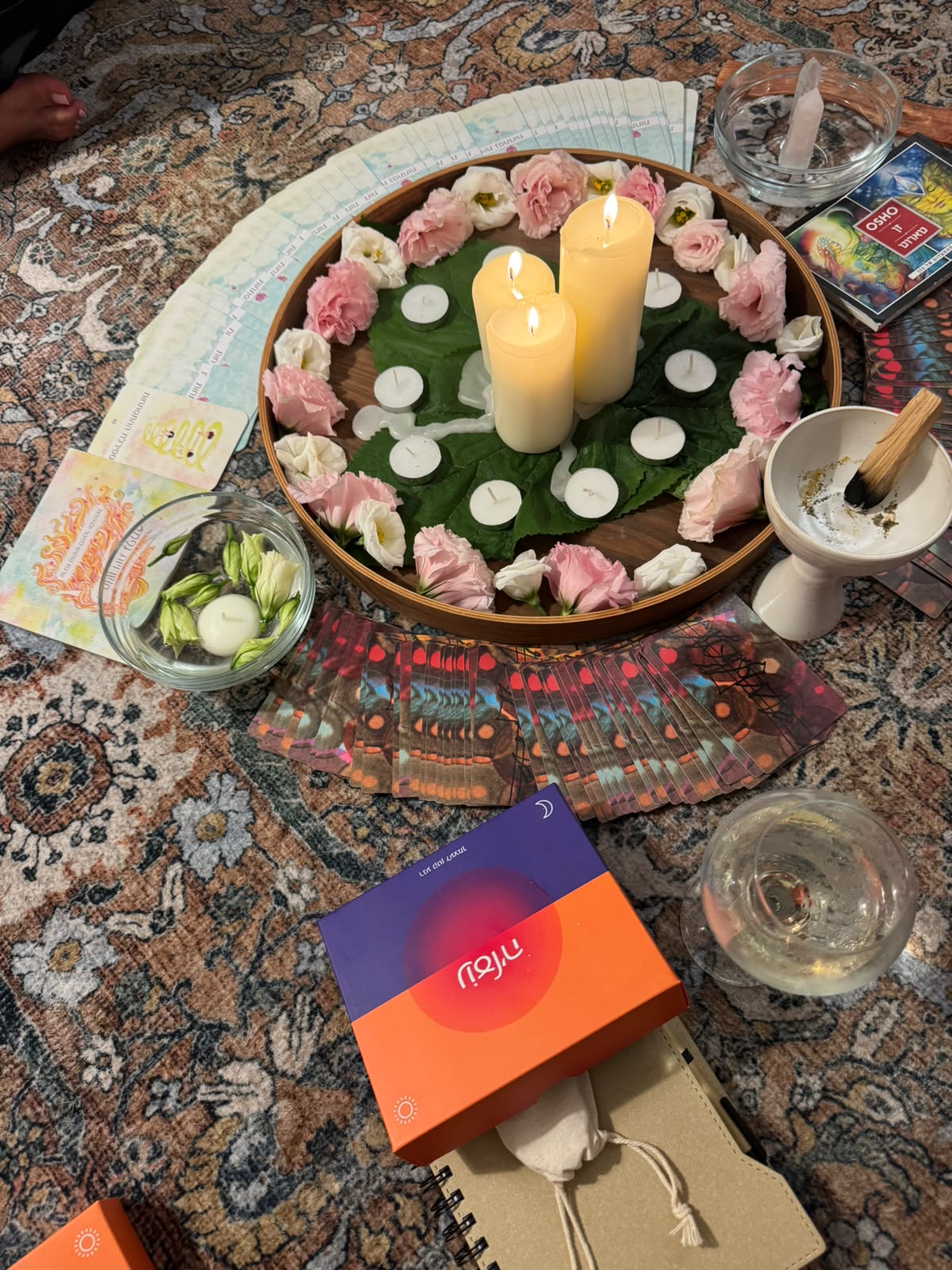 A tray with candles and pink and white flowers, cards and a bowl of palo santo